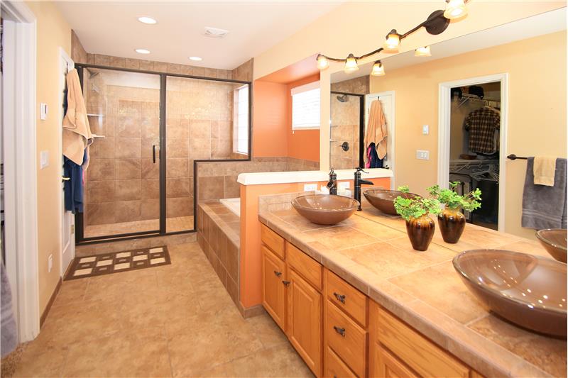 Updated master bath with heated tile floors, double vanity with vessel sink bowls, large shower with bench, jetted tub, linen cl