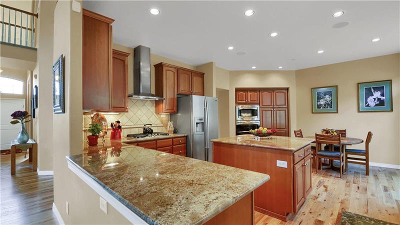 Gourmet kitchen is a chef's dream with hardwood flooring, granite counters, and tile backsplash