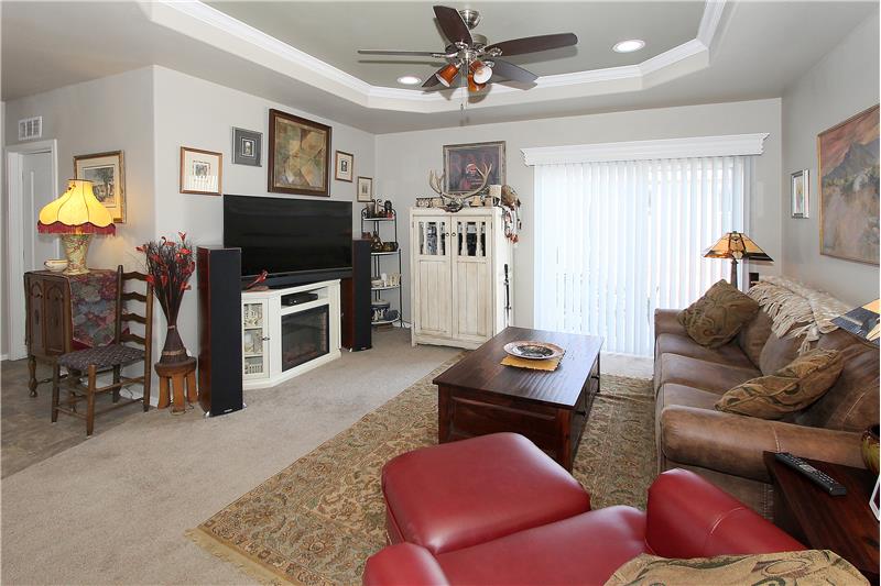 Living room with tray ceiling, recessed lighting, and ceiling fan.