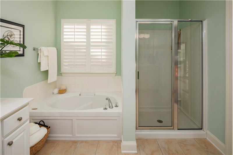 Light filters through Plantation Shutters over Oval Soaking Tub, separate glass enclosed Shower
