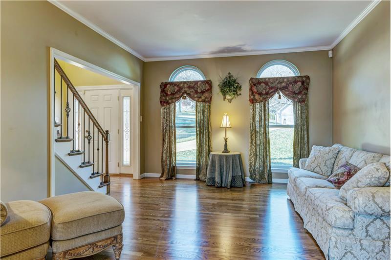 Living room with wood floor open to the family room, crown molding, palladian windows.