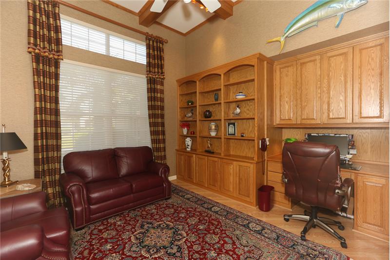 The den/office with a beautiful natural wood coffered ceiling and custom built-in solid wood cabinetry with desk can easily be u