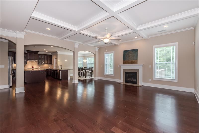 Huge great room with coffered ceiling housing recessed lights and open sight lines to the kitchen and breakfast area.